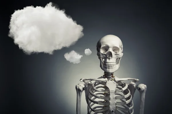 Squelette humain réfléchissant sur un fond gris — Photo