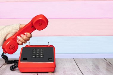 Soyut çizgili arka plan dokusunun üzerinde eski bir kırmızı telefon ahizesini tutan güzel manikürlü bir kadın eli. İletişim geçmişi. Boşluk.