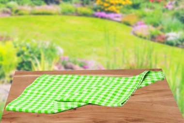 Boş masa ürünü. Soyut bulanık doğal arkaplan üzerine yeşil beyaz kareli masa örtüsüyle kaplı boş ahşap masa. Gıda ve ürün görüntüleme kurgunuz için yer.