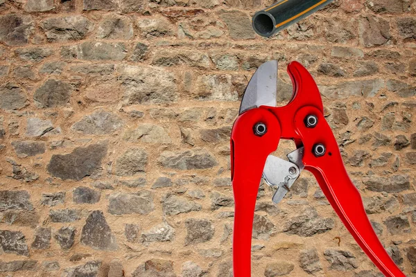 Plumber tools isolated. A red PVC pipe cutter for cutting plastic pipes and a piece of PE pressure pipe or water pipe over stone wall. Space. Craftsman tools.