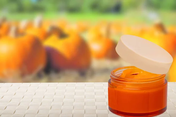 Natural cosmetics in autumn. A homemade pumpkin face mask in a glass jar on the table over blurred pumpkin background. DIY cosmetics and SPA. Copy space.