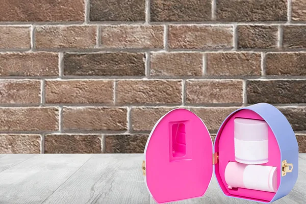 Closeup of an opened decorative cosmetic box or gift box with label-free pink white containers on a table over brick wall background. Copy space.