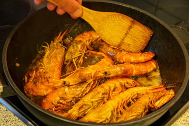 Arjantin kırmızı karidesleri. Tavada Arjantin usulü kızarmış karides ve tahta kaşıkla bir el. Sağlıklı gıda konsepti. Barbekü. Deniz ürünleri geçmişi. Alan reklamı.