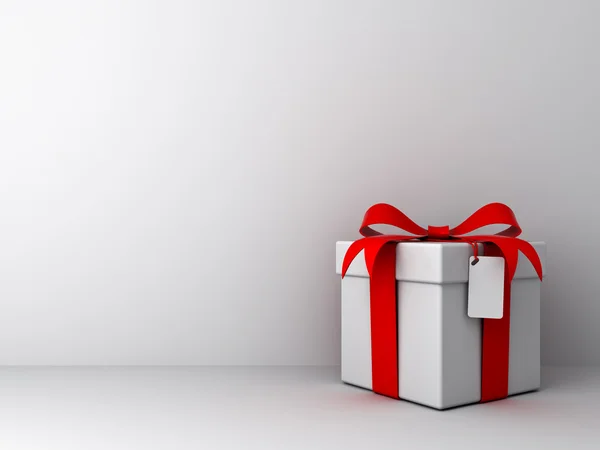 Caja de regalo con lazo de cinta roja y etiqueta en blanco sobre fondo de pared blanco vacío —  Fotos de Stock