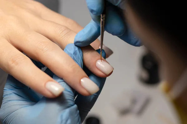 The process of doing a manicure in a spa salon. Manicurist applies milky gel polish on nails in a beauty salon. Applying gel polish. Hand care concept.