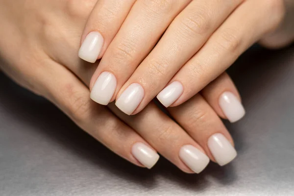 Beautiful nude manicure. Short square nails. Nail design. Manicure with gel polish. Close-up of the hands of a young woman with a delicate nude manicure on her nails. Elegant nails with gel polish.