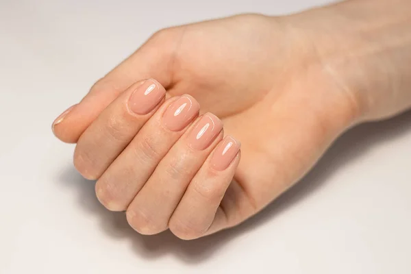 Nail care and manicure. Close-up of a beautiful female hand with nude gel polish on nails. Natural square nails. A high resolution