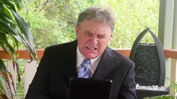 Mature businessman who is frustrated and upset sitting in a chair on a verandah. — Stock Video