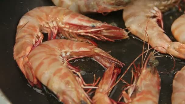 Camarones enteros se fríen en una sartén con aceite que se da vuelta con pinzas . — Vídeo de stock