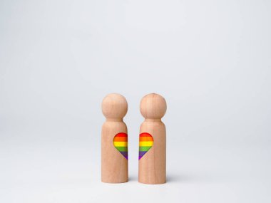 LGBT çift kavramı. İki ahşap figürün kalp şeklinde gökkuşağı bayrağı beyaz arka planda izole bir şekilde yan yana duruyor. LGBT gurur simgesi.