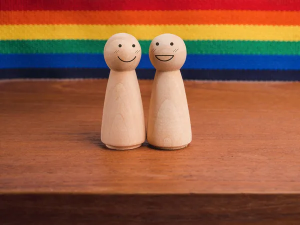 Lgbtカップルのコンセプト スカートの形をした木製の人形2体 虹の旗の背景にある木製のテーブルの上に幸せな笑顔が一緒に立っています Lgbtプライドシンボル — ストック写真