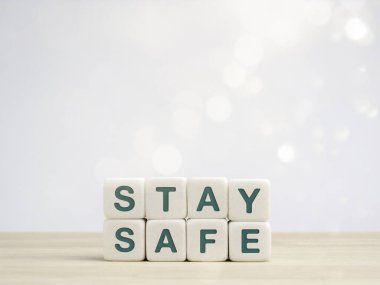 Güvenli konsept. Yeşil kelimeler, beyaz zar bloklarında tahta masada beyaz arka planda Bokeh ve kopyalama alanlarında güvende olun. Enfeksiyon riskini azaltmak ve Coronavirüs 'ü yaymak için evde kalmak.