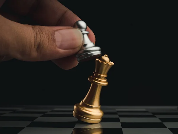 特写的小银质棋子在黑暗的背景下攻击了棋盘上的金色皇后 棋类比赛中的棋类移动手 管理和领导概念 — 图库照片