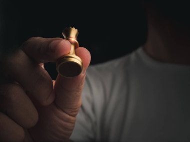 Altın kraliçe satranç taşı insan eliyle havada, arka planda fotokopi uzayı ile birlikte. Satranç müsabakasında düşmana saldırmaya hazır el hareketli kraliçe satranç figürü. Kazanan Liderlik konsepti.