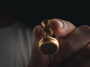 Altın kraliçe satranç taşını insan eliyle kaplayın. Karanlık arka planda, görüş açısının altında. Satranç yarışmasında el hareketli kraliçe satranç figürü. Kazanan Liderlik konsepti.