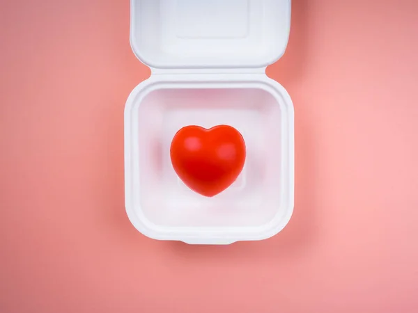 ピンクのパステルの背景に白い正方形の紙の食品箱に赤いハートボール 最小限のスタイル 分かち合い 食糧供給 寄付の概念 — ストック写真