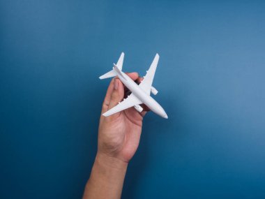 Mavi arka planda el ele tutuşan beyaz bir oyuncak model, üst manzara, minimal stil. Beyaz uçak, düz dizayn. Uçuş, seyahat konsepti.