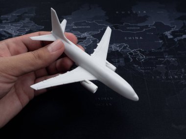 Dünya haritası arka planında beyaz uçağın oyuncak modelini tutan yakın plan, üst görünüm, minimal tarz. Uçuş, seyahat, varış ve yolculuk konsepti.