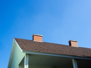 Güneşli bir günde, açık yeşil ahşap evin çatısındaki iki bacayı mavi gökyüzü arka planına karşı kapatın..