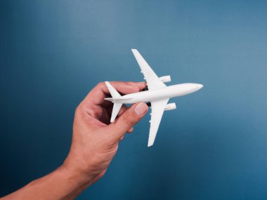 Mavi arka planda el ele tutuşan beyaz bir oyuncak model, üst manzara, minimal stil. Beyaz uçak, düz dizayn. Uçuş, seyahat konsepti.