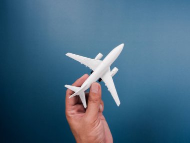 Mavi arka planda el ele tutuşan beyaz bir oyuncak model, üst manzara, minimal stil. Beyaz uçak, düz dizayn. Uçuş, seyahat konsepti.
