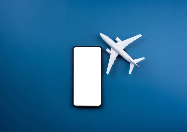 青い背景に白いきれいな飛行機モデルのおもちゃとスマートフォン上の白い空白の画面のモックアップ 携帯電話アプリ オンライン旅行 バケーション保険のコンセプトで航空券の予約 — ストック写真