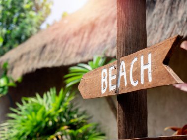 Plaj yolu tabelası. Beyaz metin, ahşap tabelada plaj ya da otel odunluğundaki tahta direğin üzerinde ok şeklinde bir tabela. Kumsala giden tahtadan bir işaret..