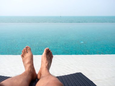 Tropikal havuz ve deniz manzaralı mavi sularda güneşlenirken adamın ayağının yakın çekimi. Tatil, yaz tatili arkaplanı kopyalama alanı.