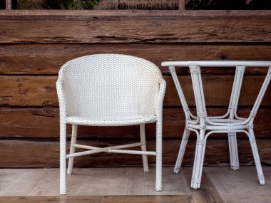 Boş modern beyaz rattan mobilyalar, açık hava bahçe dokuma sandalyesi ve terasın arka planındaki tahta odunların üzerine yuvarlak masa..