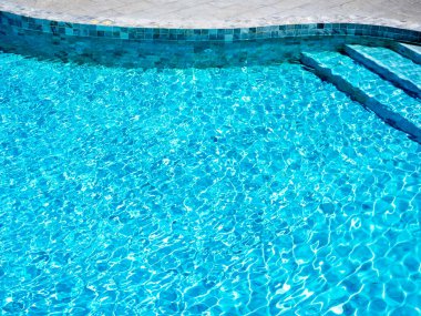 Temiz ve berrak mavi su yüzeyi kıvrımlı yüzme havuzunun arka planındaki ışıkla hareket dalgası parlıyor. Yaz arkaplanı için boş alan, tatil izni, tatil kavramı.