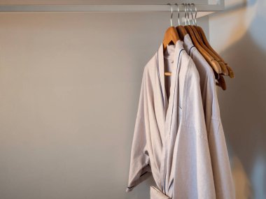 Beyaz gardıroptaki askılarda asılı duran birkaç Japon tarzı pamuk bornoz. Loş ışıklarda fotokopi çekilen otel misafirleri için..