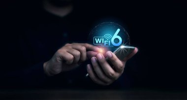 Wi-Fi 6 logosu cep telefonunda görülürken iş adamının eli onu karanlık arka planda kullanıyordu. Akıllı performansı olan yeni nesil telekomünikasyon bağlantı ağı.