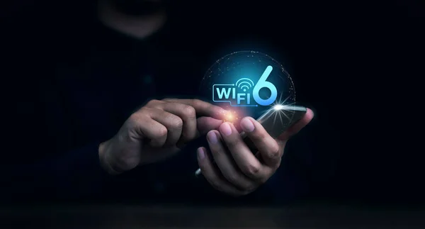 Wi-Fi 6 logo virtual appeared on mobile smartphone while business man\'s hand using it on dark background. New generation telecommunications connectivity network with smart performance.