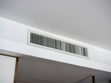 Beyaz otel odasının tavanına havalandırma duvarı monte edilmiş. Otel odasının havalandırma ızgarası duvarda..