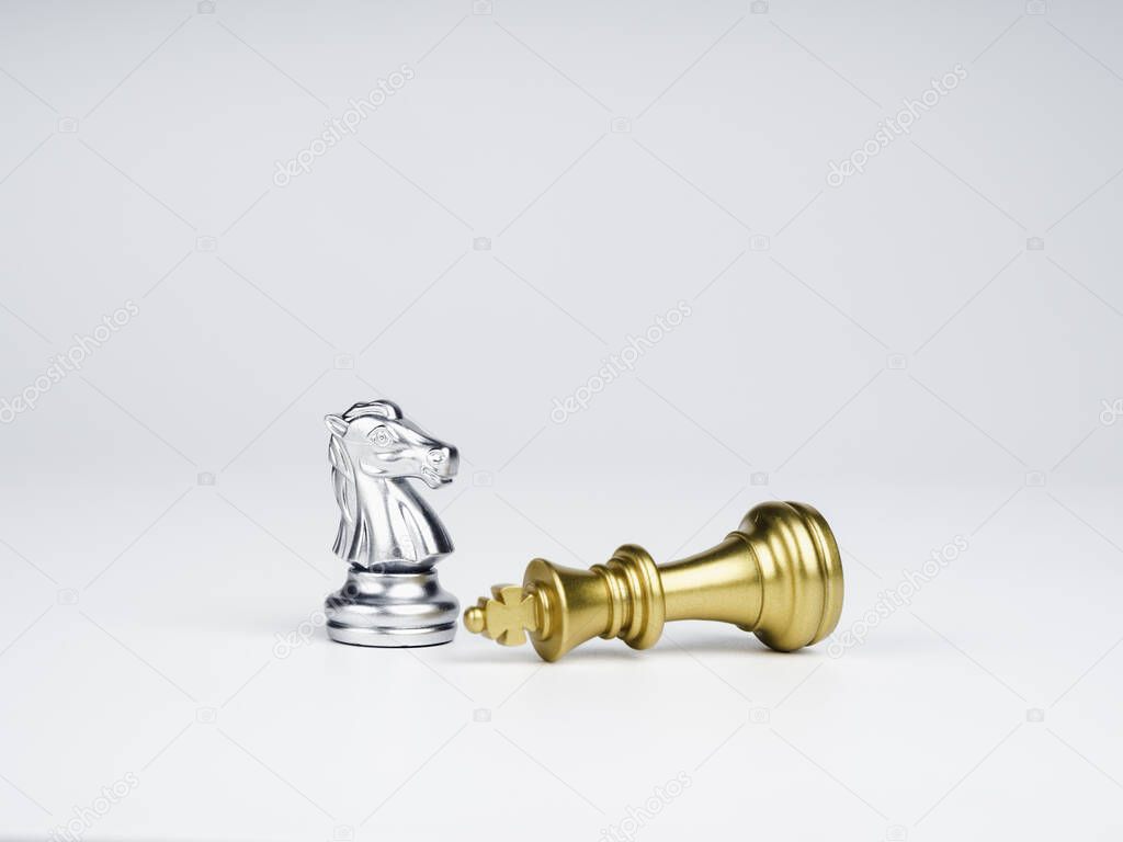The silver horses, knight chess piece standing near the loser golden king chess piece who fell isolated on white background. Leadership, winner, loser, competition, and business strategy concept.
