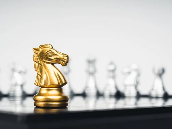 The golden horse, knight chess piece stand alone in front of silver chess pieces on chessboard on white background. Leadership, fighter, surviver, competition, and business strategy concept.