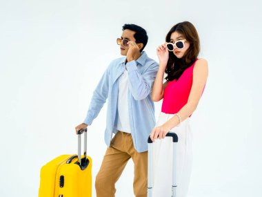Yolculuğa hazırız, iyi tatiller. Yaz tatili kavramı. Asyalı çift neşeli bir şekilde güneş gözlüğü takıyor ve heyecanlı bir şekilde ileriye bakıyor. Yolculukta bavullu kadın ve erkek, beyaz arka planda izole edilmiş..