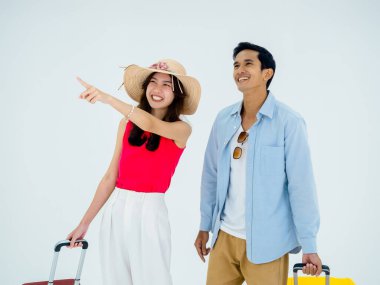 Heyecan verici bir yolculuk, mutlu tatiller. Yaz tatili. Asyalı çift gezginler, heyecan verici, gülümseyen bir adam ve genç bir bayanla jestler yapıp, beyaz arka planda izole bir şekilde seyahat ederken bavullarını gösteriyorlar..