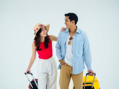 Birkaç gezgin, arkadaşlarla mutlu tatiller. Yaz tatili. Renkli kostümler içinde genç Asyalı erkek ve kadın gülümseyerek birbirlerine bakıyorlar, beyaz arka planda izole edilmiş bavullarla yürüyorlar..