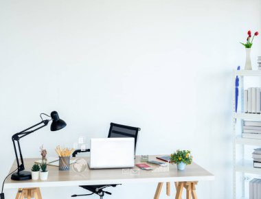 Modern workplace with business icon virtual near laptop computer, pencil, notebook table lamp, cash, credit card and passport on wood desk near the bookshelf on white wall background with copy space.