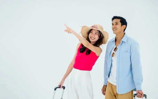 Exciting travel, happy holiday. Summer vacation. Asian couple travelers looking out with exciting, Man and young woman pointing with suitcases on trip with copy space, isolated on white background.