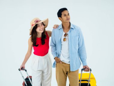 Birkaç gezgin, arkadaşlarla mutlu tatiller. Yaz tatili. Renkli kostümler içinde genç Asyalı bir adam ve kadın gülümsüyor, beyaz arka planda izole edilmiş bavullarla yürüyor..