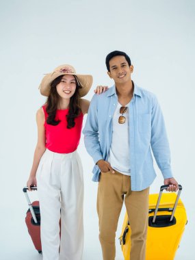 Birkaç gezgin, arkadaşlarla mutlu tatiller. Yaz tatili. Renkli kostümler içinde genç bir Asyalı adam ve kadın kameraya bakıyor, beyaz arka planda izole edilmiş bavullarla yürüyorlar, dikey tarzda..