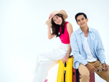 Seyahate hazır iki yolcu, iyi tatiller. Renkli bir yaz tatili. Plaj şapkalı genç, Asyalı bir kadın, kot gömlekli bir adam, beyaz arka planda izole edilmiş sarı bavullarda birlikte oturuyor..