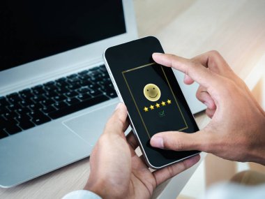 Gülen yüz ve beş yıldız puanı. Akıllı cep telefonu ekranında en iyi değerlendirme. İnsanlar tarafından çevrimiçi memnuniyet. Müşteri hizmetleri değerlendirmesi, müşteri deneyimi araştırma kavramı.