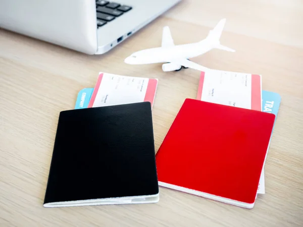 黒と赤 2つのパスポートの異なる色で ノートパソコンの近くの2つのフライトチケットと日光のある机の上の飛行機のおもちゃで覆われています 旅行のコンセプトのためのオンラインチケット予約 — ストック写真