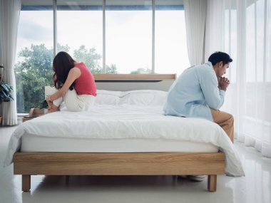 Yataktaki Asyalı çiftlerin endişeleri. Düşünceli bir adam ve genç bir kadın ilişki zorlukları içinde yatakta oturuyor üzgün hissediyor ve cam pencerenin yanındaki yatak odasında düşünüyor..