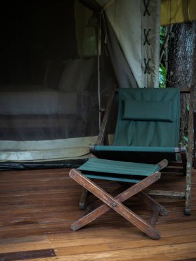 Boş kamp ahşap koltuğu, yeşil kumaş koltuğu ve büyük çadırın önündeki terasta ayak dinlenme yeri. Beyaz glamping çadırı üzerinde katlanır güneş yatağı, dikey stil.