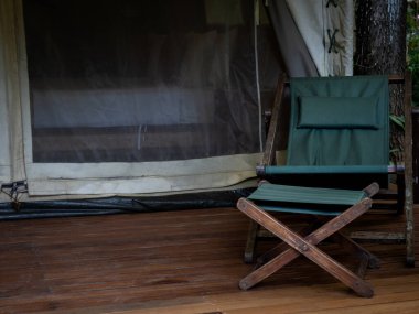 Boş kamp ahşap koltuğu, yeşil kumaş koltuğu ve büyük çadırın önündeki terasta ayak dinlenme yeri. Beyaz glamping çadırında güneşlenmek..