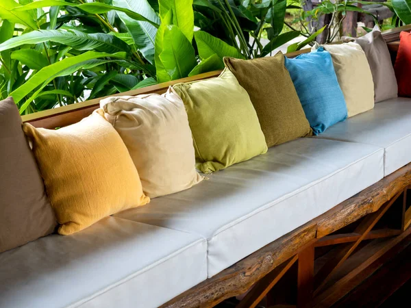 Row of many color of pillows decoration on the vintage wooden seat with white pads near the green garden.